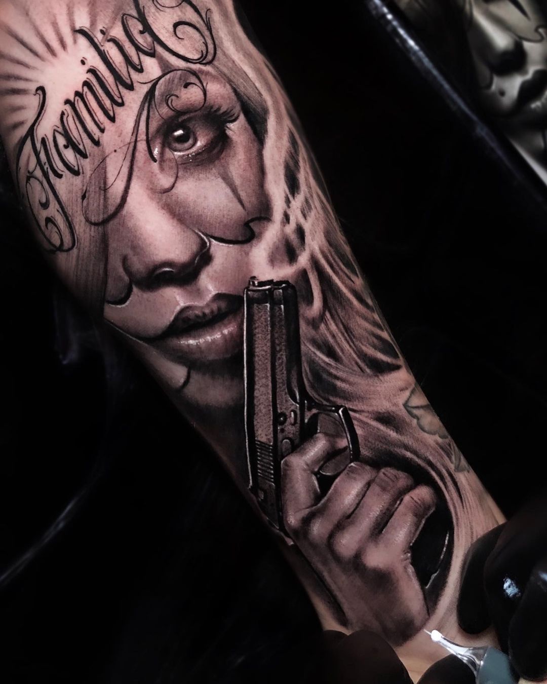 Chicano tattoo van een vrouw met een pistool en sierletters op een onderarm